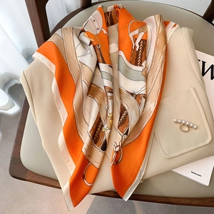Luxurious orange silk scarf with equestrian prints and beige vest on a leather chair
