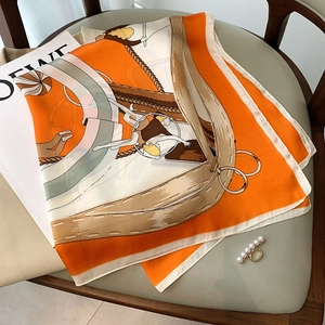 Orange and cream satin square scarf with circus print and silk-like texture on chair