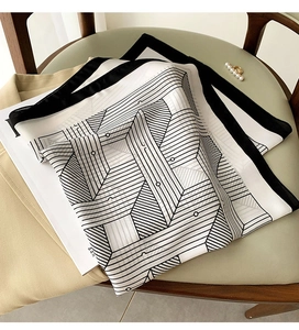 Close-up of a black and white geometric silk scarf draped on a chair with a beige blazer