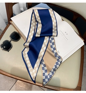 Detail of a navy and beige silk twilly scarf with geometric letter patterns on a book