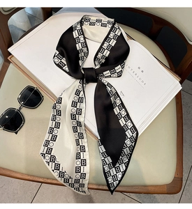 Detail view of a black and white twilly silk scarf featuring repeated letter patterns