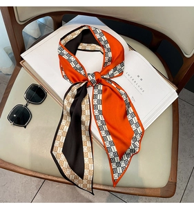 Close-up of a silk-feel orange and black letter print scarf styled on a book with sunglasses