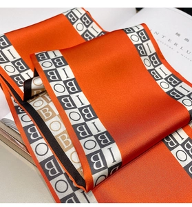Macro detail of silk-like orange scarf featuring geometric B pattern and glossy texture