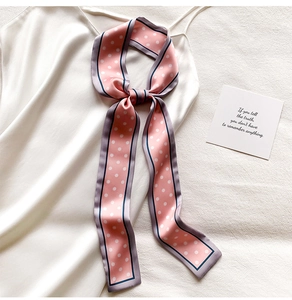 Gros plan d'un foulard en soie rose à pois noué sur une robe blanche, texture satin