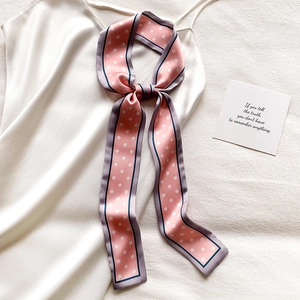 Écharpe étroite en soie rose à pois nouée en nœud sur une robe en satin blanc