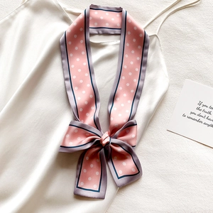 Détail d'un foulard en soie rose à pois noué en nœud sur un vêtement en satin blanc