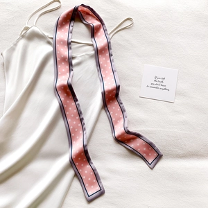 Détail d'un foulard en soie rose à pois drapé sur du satin blanc au fini soyeux doux