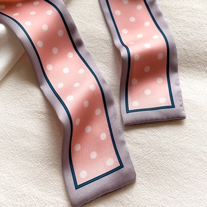 Gros plan d'un foulard en soie rose à pois avec bords lilas sur tissu beige