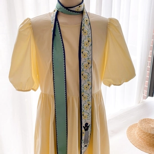 Détail d'un petit foulard en soie à imprimé floral porté avec une robe jaune