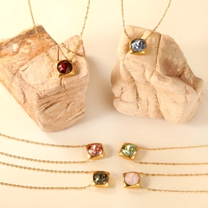 Golden square stone necklaces in assorted colors like burgundy and opal displayed on stones