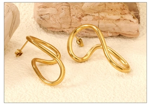 Macro shot of abstract wavy gold earrings on natural stone background with light shadows