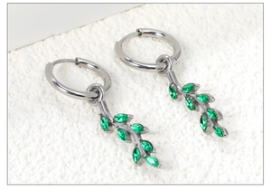 Detail of silver leaf earrings featuring green marquise zircon stones on stone surface