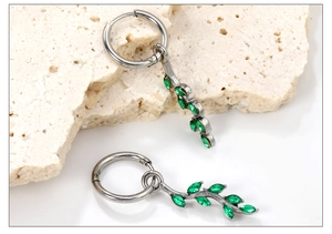 Detail view of silver leaf earrings with green marquise stones on stone surface