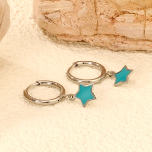 Detail view of silver hoop earrings featuring green star charms on a textured stone surface
