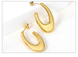 Détail de boucles d'oreilles épaisses en forme de U dorées sur un fond blanc minimaliste