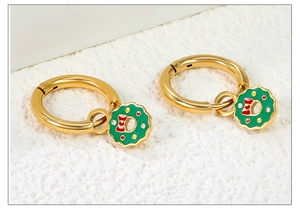 Détail de créoles dorées avec pendentif couronne de Noël verte et nœud rouge