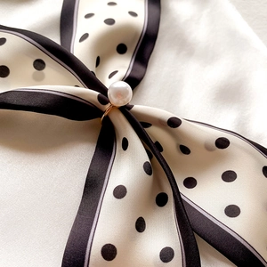 Gros plan d'une boucle de foulard en perle dorée sur un foulard en soie à pois noir et blanc