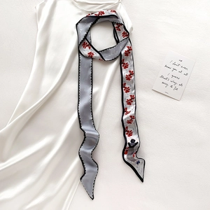 Détail d'un foulard twilly à imprimé floral rouge sur robe en satin à texture lisse