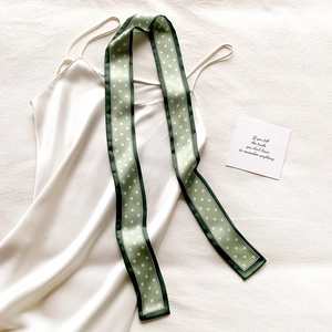 Détail d'un foulard en soie vert clair à pois drapé sur une robe blanche élégante