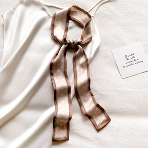 Détail d'un foulard étroit à pois champagne noué sur une robe en soie blanche