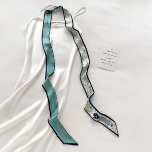 Détail d'un foulard twilly double face avec texte vert menthe et motifs floraux jaunes