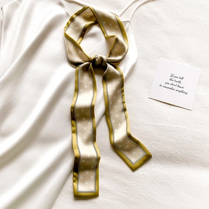 Détail d'un foulard étroit en satin à pois champagne noué sur un caraco en soie blanche