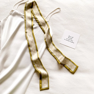 Vue à plat d'une robe en satin crème avec un foulard en soie à pois vert olive élégant