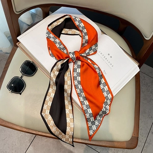 Stylish silk twilly scarf with orange and black letter print styled on a white magazine