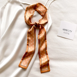 Détail du foulard en soie orange à pois drapé sur une robe blanche au fini soyeux