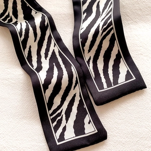 Detail of narrow zebra pattern silk scarf tied as a luxury bag handle accessory