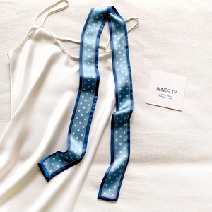 Détail d'un foulard en soie à pois bleus et blancs noué sur une robe élégante