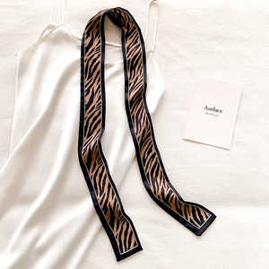 Detail of leopard print narrow silk scarf styled with a white satin dress on beige fabric