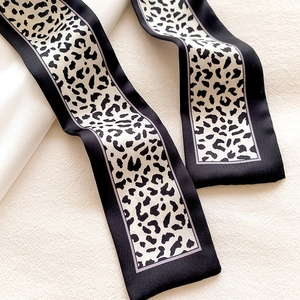Close-up of leopard print skinny silk scarf with black borders on soft fabric
