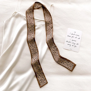 Close-up of leopard print satin skinny scarf paired with a white silk slip dress