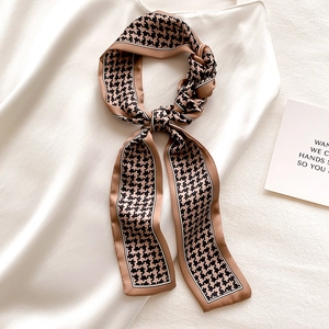 Close-up of a classic houndstooth skinny scarf in coffee and black silk-like fabric