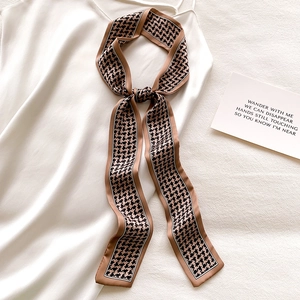 Detail of a brown houndstooth skinny scarf tied on a white silk dress as a stylish belt