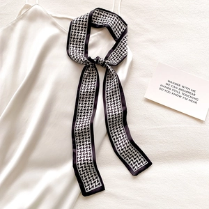 Close-up of black and white houndstooth skinny silk scarf tied on a white satin strap