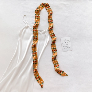 Close-up of geometric pattern silk twilly scarf tied on a white satin strap dress