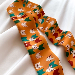 Detailed view of orange twilly scarf with green and red geometric arrow patterns
