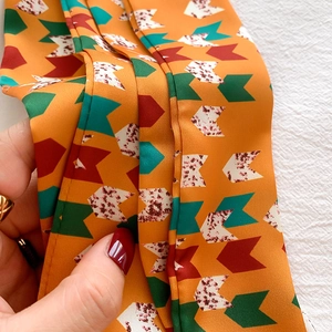 Detail of soft silk-like satin scarf with orange geometric patterns and tail finish