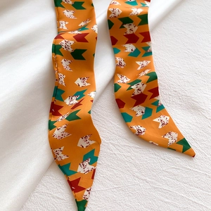Close-up of geometric silk twilly ribbon with orange arrow patterns on white fabric