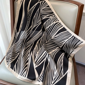 Elegant striped silk scarf with black leaf veins draped on a leather chair