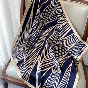 Close-up of navy blue silk square scarf with beige leaf patterns draped over a wooden chair