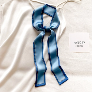 Détail d'un foulard étroit bleu ciel noué en boucle sur un vêtement en satin