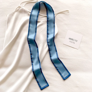Détail d'un foulard étroit en soie bleue avec bordures blanches sur fond de satin blanc
