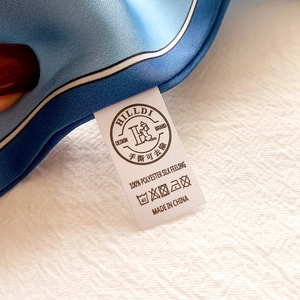 Détail d'un foulard bleu au toucher soie avec étiquette 100% polyester et passepoil fin