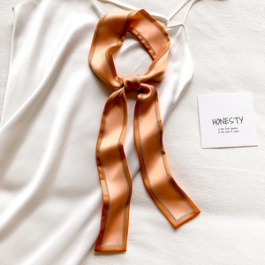 Détail d'un foulard en soie orange vif avec bordures noires et blanches sur tissu