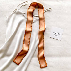 Gros plan d'un foulard en soie orange-rose rayé sur une robe nuisette en satin blanc
