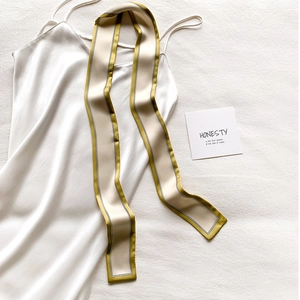 Détail d'un foulard en soie beige et vert olive sur une robe en satin blanc