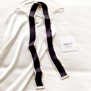 Détail d'un foulard étroit noir en satin avec liseré crème sur une robe en soie